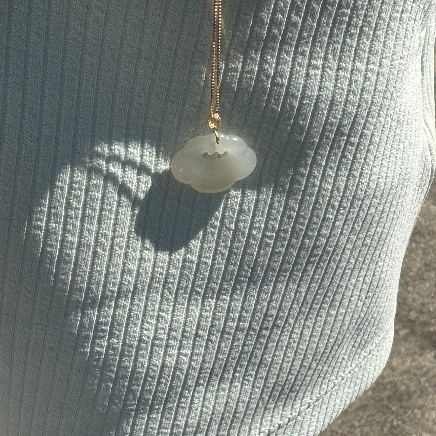 Lucky Cloud White Jade Necklace sparkling under the sunlight, highlighting the soft glow of white jade and 18k gold details on a gold-plated chain.