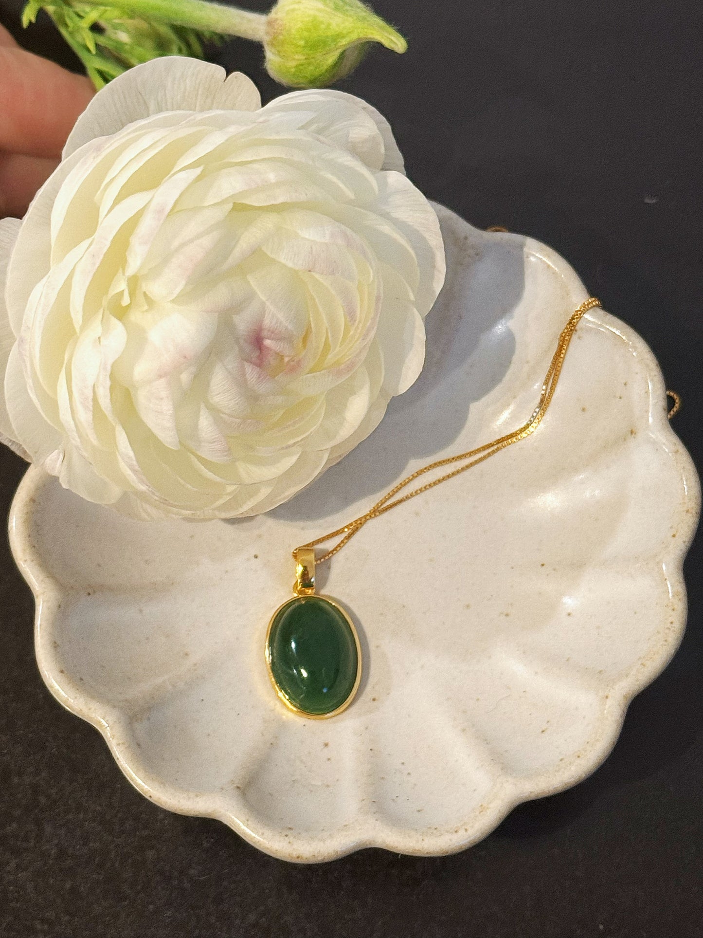 Oval green Jade Necklace with gold-plated 925 silver chain styled beside a white flower, highlighting its timeless elegance and natural beauty.